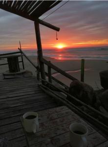 two coffee cups sitting on a dock with a sunset at Balcon Del Tigre in Aguas Dulces