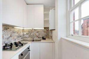 Biała kuchnia z białymi szafkami i oknem w obiekcie Beaufort Gem Chelsea Apartment w Londynie