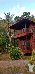 a red house with a balcony and a palm tree at Eco Cabanas Marakolliya in Tangalle