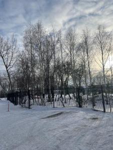 Una valla negra en la nieve con árboles detrás. en Апартаменты Promenade Burabay, en Burabay