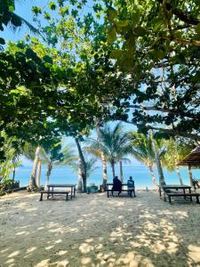 zwei Personen sitzen auf Bänken am Strand mit Bäumen in der Unterkunft Sunny Cove Beach Resort Koh Phayam in Ranong