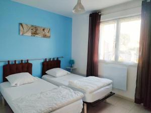 Duas camas num quarto azul com uma janela em Maison Cosy à proximité de la Plage em Hermanville-sur-Mer