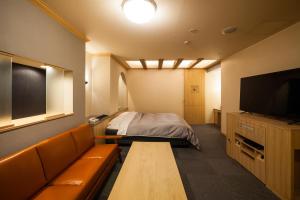 a room with a bed and a couch and a television at Hotel Torni ホテル トルニ in Toyama