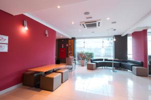 a waiting room with a red wall and tables and chairs at ibis Presidente Prudente Manoel Goulart in Presidente Prudente