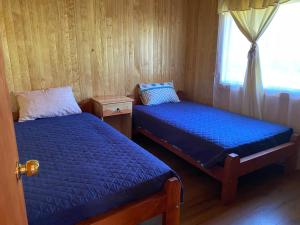 two beds in a small room with a window at Cabaña Llonquén in Liquiñe