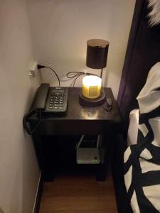 - une table de chevet avec une lampe et un téléphone à côté d'un lit dans l'établissement Rm’s Inn, à Manille