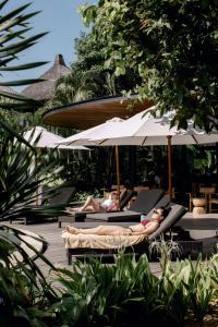 een groep mensen die op ligstoelen onder parasols liggen bij Wave House - Surf Camp in Canggu