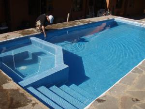 un hombre de pie junto a una piscina azul en Apart Hotel Del Arroyo en San Carlos de Bariloche