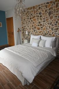 a bedroom with a large white bed with a stone wall at Aux 3 Forêts in Bizeneuille