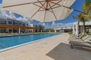 una piscina con sombrilla y tumbonas junto a un edificio en Apartamento 2 habitaciones piscina cerca de playa, en Punta Cana