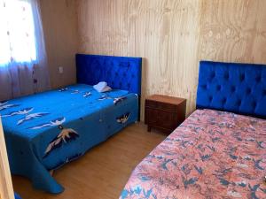 a bedroom with two beds with blue covers and a table at PICHIDANGUI, Cabañas Las Golondrinas in Pichidangui