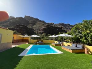 a swimming pool with chairs and umbrellas and a mountain at SUNNY CARMELITO DELUXE in Mogán