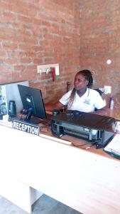 una mujer sentada en un escritorio con un ordenador en dunduzu village lodge, en Mzuzu