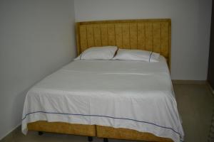 een bed met een houten hoofdeinde en witte lakens bij Casa Campo Villa Rosa in Valledupar