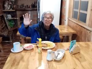 an older man sitting at a table with his hand in the air at Hostal Ñuca Huasi in Tambillo