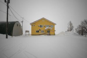 una casa amarilla en la nieve en una calle nevada en THE NORTH PEAK NAKAFURANO, en Nakafurano