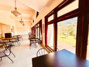 uma sala de jantar com mesas e cadeiras e janelas grandes em Sagar Heritage Resort, Manali em Manali