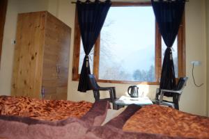 a bedroom with a bed and two chairs and a window at Apple Garden Katagla Kasol in Kasol