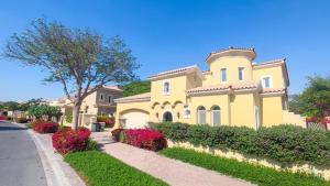 a yellow house with a landscaping in front of a street at Luxury 3BR Villa with Assistant Room at Alvorada 4 Arabian Ranches by Deluxe Holiday Homes in Dubai