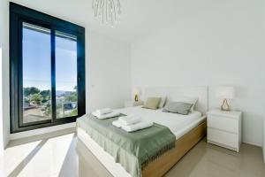 Dormitorio blanco con cama y ventana grande en Esmeralda - By Almarina Villas, en Benissa