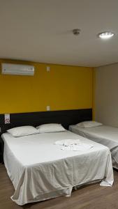 2 camas en una habitación con una pared amarilla en Ônix Inn Hotel Cravinhos, en Cravinhos
