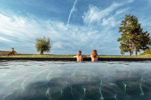 duas mulheres sentadas numa piscina de água com uma girafa ao fundo em Domaine Villoire em Cassagnes