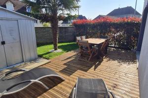 een houten terras met een tafel en stoelen erop bij Maison avec jardin. in Troarn