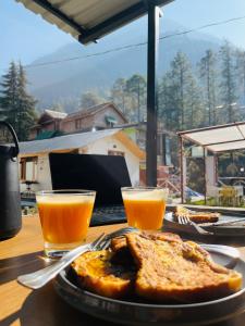 uma mesa com um prato de torradas e dois copos de sumo de laranja em Adinova em Kasol