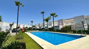 a swimming pool in front of a building with palm trees at Villa Bosque Novo Sancti petri Grupo AC Gestión in Chiclana de la Frontera