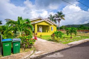 a yellow house with two trash cans in front of it at Ocho Rios Drax hall Manor 3 Bed sleeps 7 in Saint Annʼs Bay