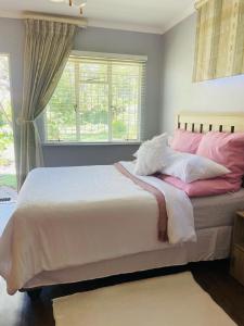 a bedroom with a large bed with pink and white pillows at The M-Pire Cottage in Bloemfontein
