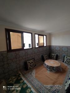 sala de estar con mesa y algunas ventanas en Maison Lahoucine, en Sidi Ifni