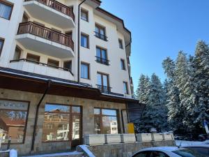a tall white building with windows and a parking lot at Forest Apartment/ Villa Park in Borovets