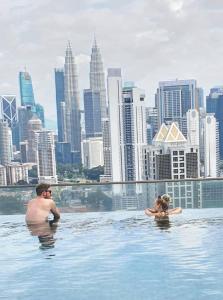 Un uomo e una donna che nuotano nell'acqua con un panorama urbano di Regalia Suites KLCC View Rooftop Infinity Pool by Angkasa Homes a Kuala Lumpur