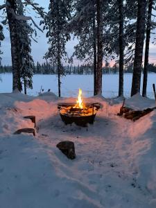 un pozo de fuego en la nieve frente a un lago en Pine Tree Cabin, en Glommersträsk