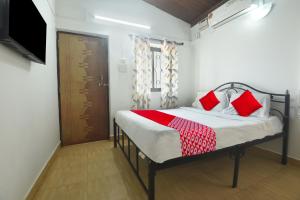 een slaapkamer met een bed met rode kussens en een televisie bij OYO Pratisha Guest House in Baga