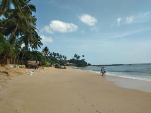 two people walking on the beach near the ocean at Sandhara Home Stay in Tangalle