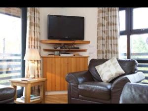 a living room with a leather couch and a flat screen tv at The Crannog on Loch Tay in Morenish