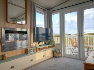 a living room with a flat screen tv and a balcony at Little Curlew, Ynyslas, Borth in Borth