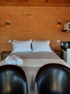 a bed with two white pillows and two chairs at Pousada Paraíso dos Pampas in Lajeadinho