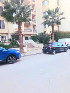 two cars parked in front of a building with palm trees at Les jardins du lac 2 in Tunis