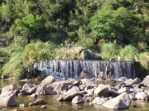 eine Gruppe von Menschen, die im Wasser in der Nähe eines Wasserfalls stehen in der Unterkunft ARROYO SERRANO-MINA CLAVERO in Mina Clavero