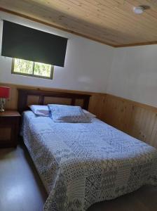 - une chambre avec un lit doté d'une couette bleue et d'une fenêtre dans l'établissement Cabañas Precordillera Radal 7 tazas, à El Torreón