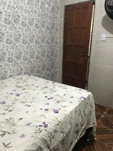 a bed with a white blanket with purple flowers on it at Michele in São Pedro da Aldeia