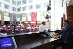 two men standing at a counter in a hotel lobby at Novotel Dammam Business Park in Dammam