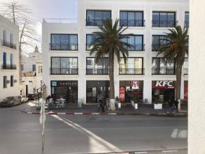 a white building with palm trees in front of a street at Jade au cœur de la Marsa plage in La Marsa