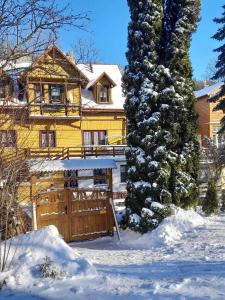 een geel huis met een houten hek in de sneeuw bij Chata i Mostek in Krynica Zdrój