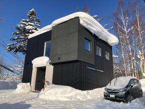 NISEKO EPIC HOUSE في نيسيكو: منزل أسود مع سيارة متوقفة في الثلج