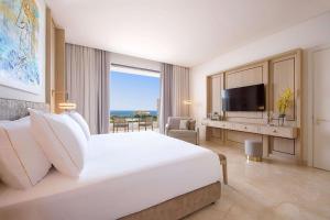 a white bedroom with a large bed and a television at Cap St Georges Hotel & Resort in Peyia