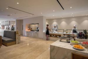 a woman standing in a kitchen with chefs preparing food at Cap St Georges Hotel & Resort in Peyia